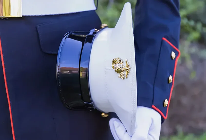 Close-up of a U.S. Marine Corps dress uniform holding a white peaked cap with gold emblem
